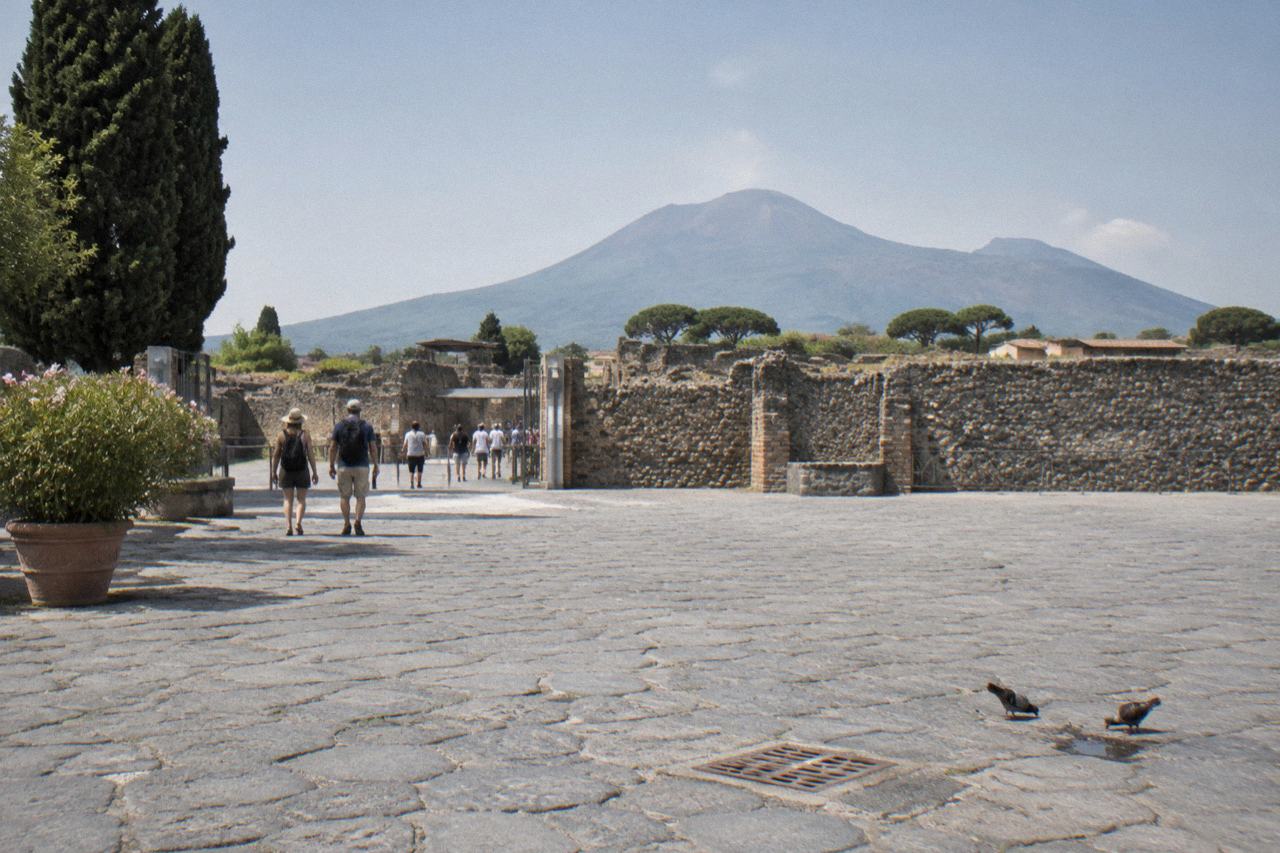 Pompeii forum ruins with the Vesuvius cone looming behind under a clear sky