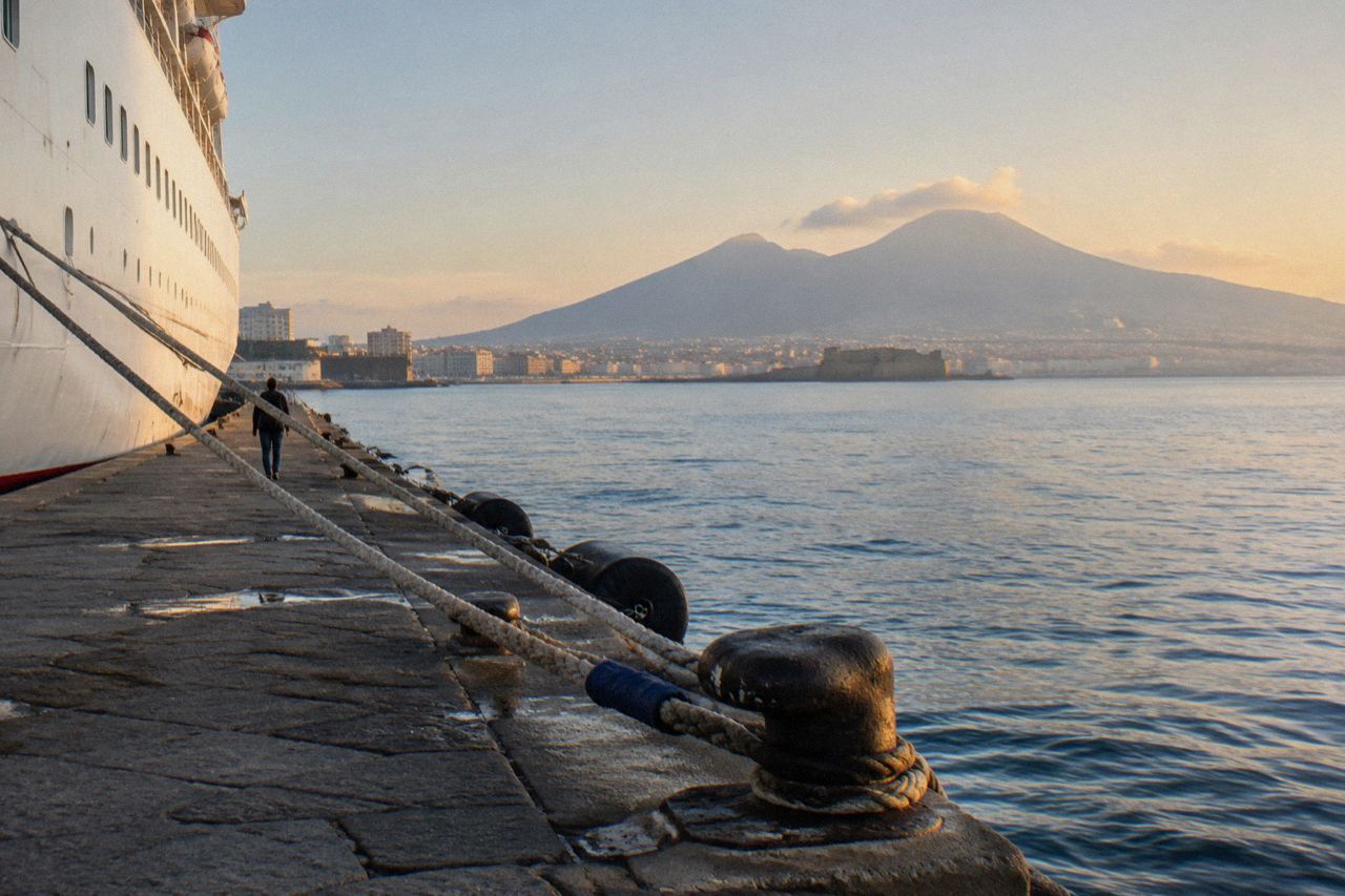 Cruise ship docked in the Port of Naples with Mount Vesuvius visible across the bay in morning light