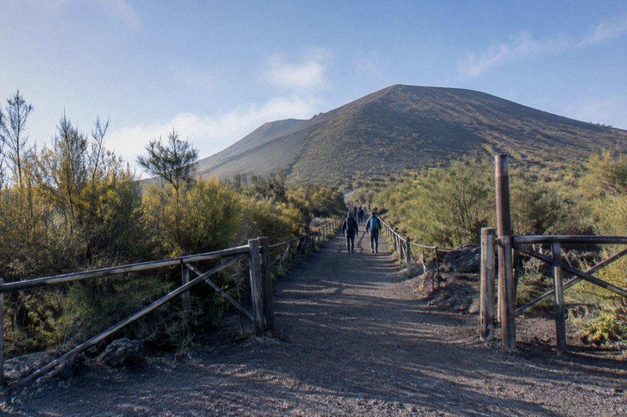 Visitors walking up the gravel path at the Vesuvius National Park entrance gate, trail and cone ahead
