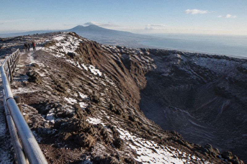 Vesuvius crater rim with a thin dusting of snow and low winter sun, a few hikers in warm jackets