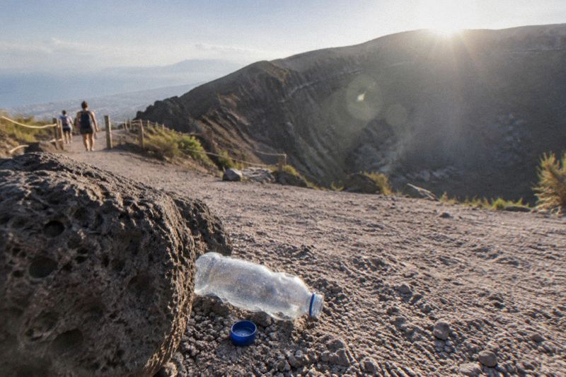 Vesuvius crater rim in strong July sun with heat haze, hikers with water bottles on the gravel path