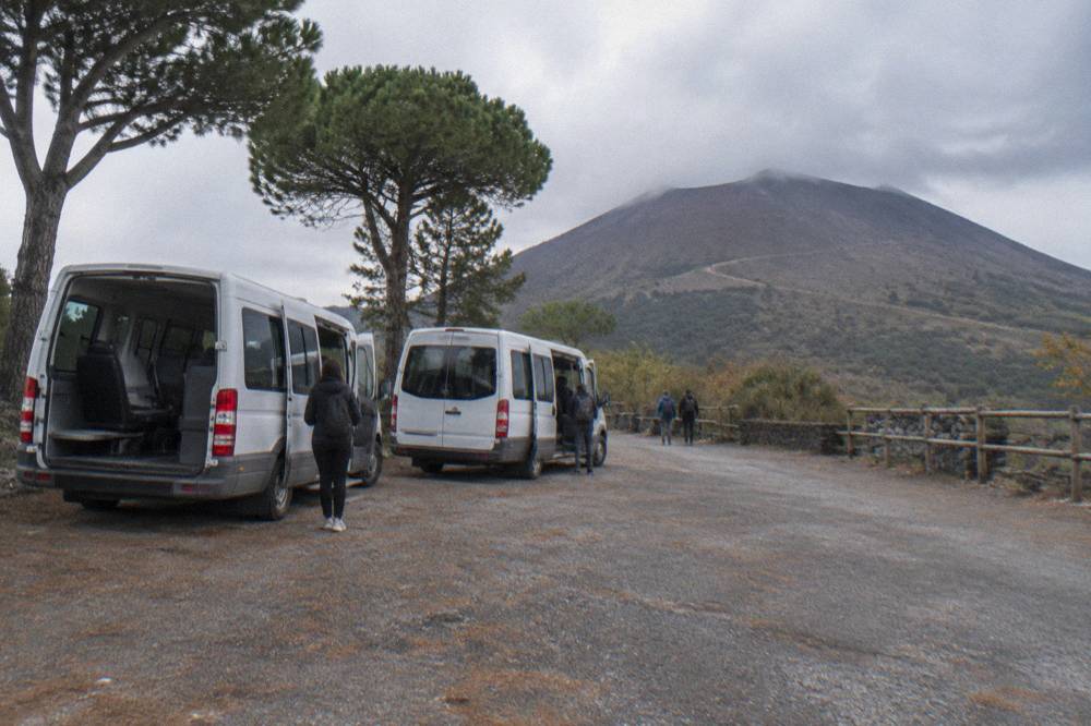 Shuttle minibuses parked at a gravel staging area on the slopes of Vesuvius