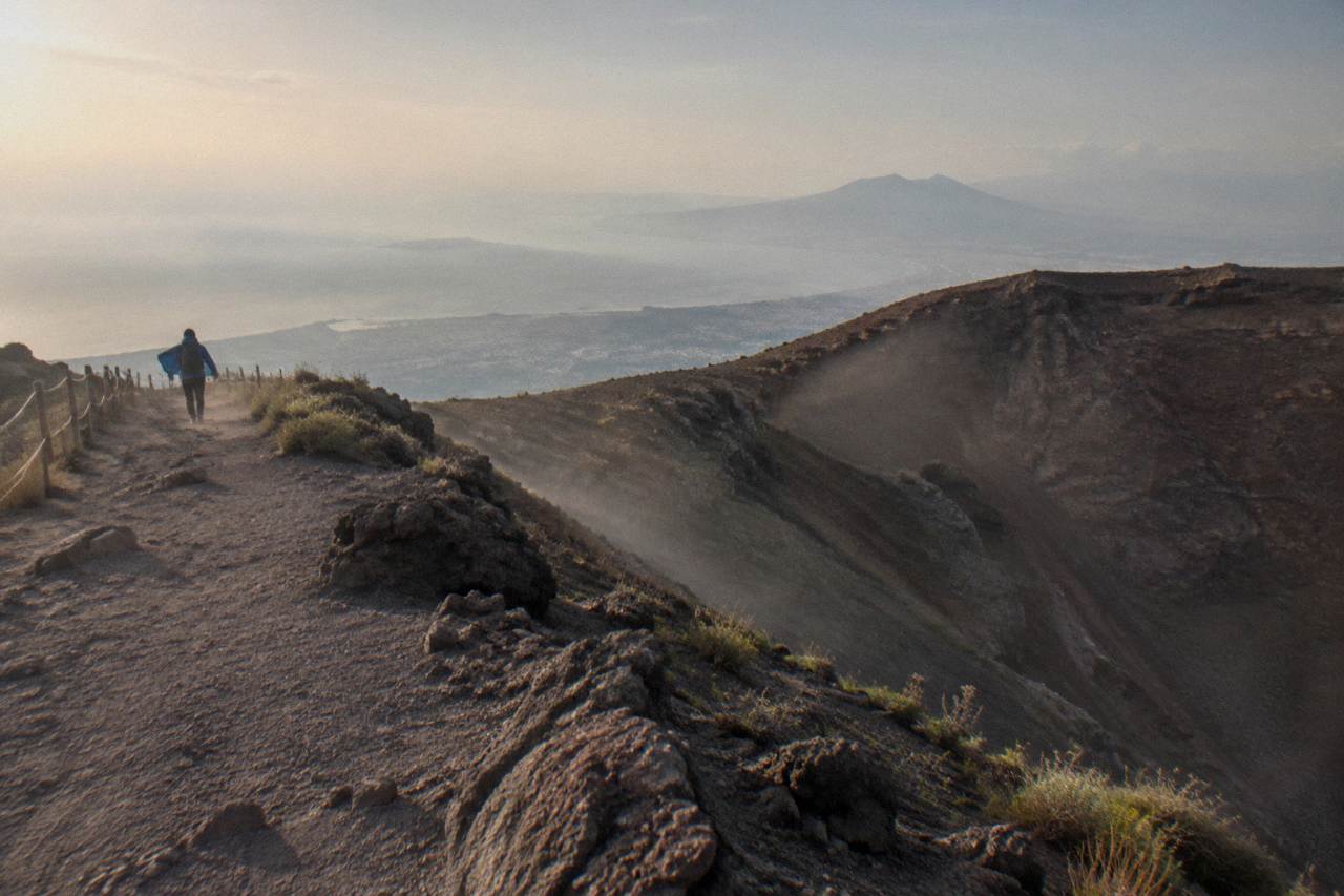 Rocky crater trail on Mount Vesuvius under a wide sky with the Bay of Naples far below