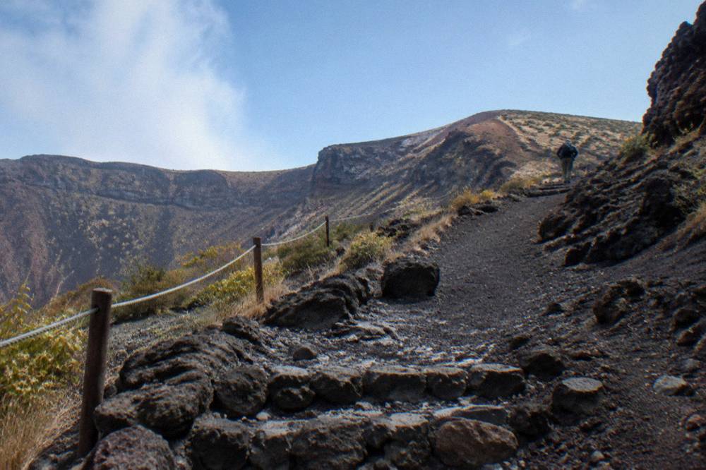 Walking path of dark volcanic ash rising toward the rim of the Vesuvius crater under a clear sky