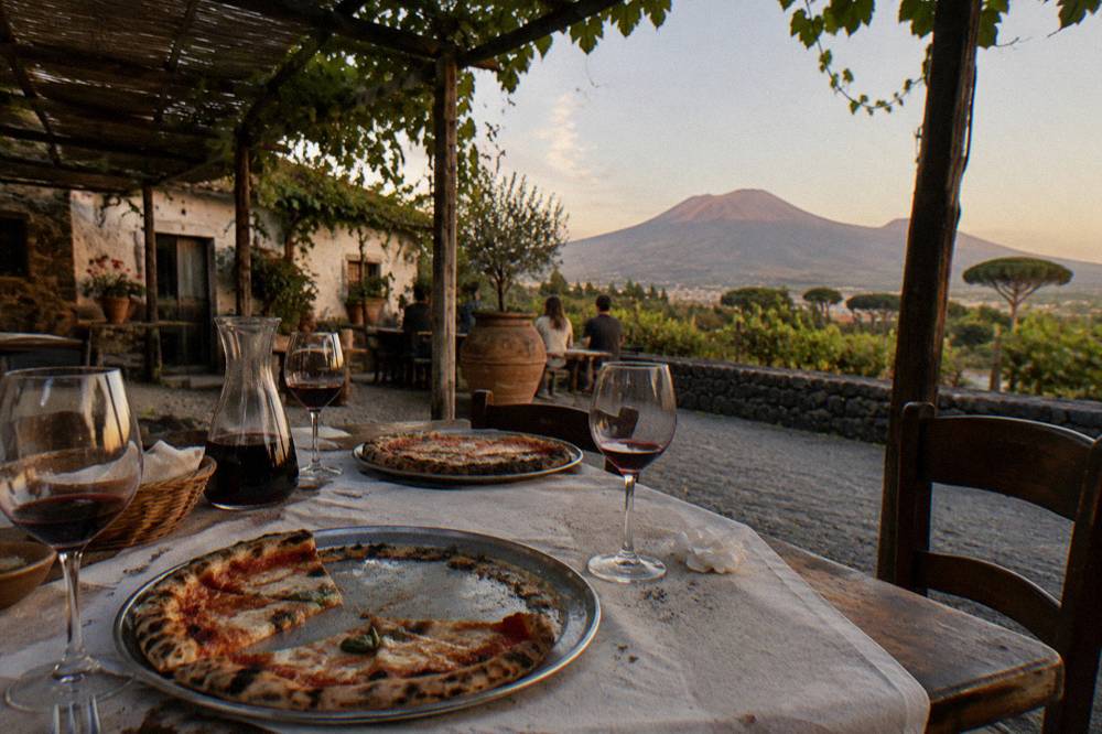 Wooden pizza trays and wine glasses on a rustic table at a Vesuvius slope farmhouse
