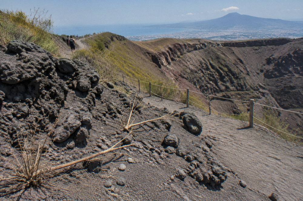 Rough black lava rock and grey ash covering the slopes of Mount Vesuvius near the crater path