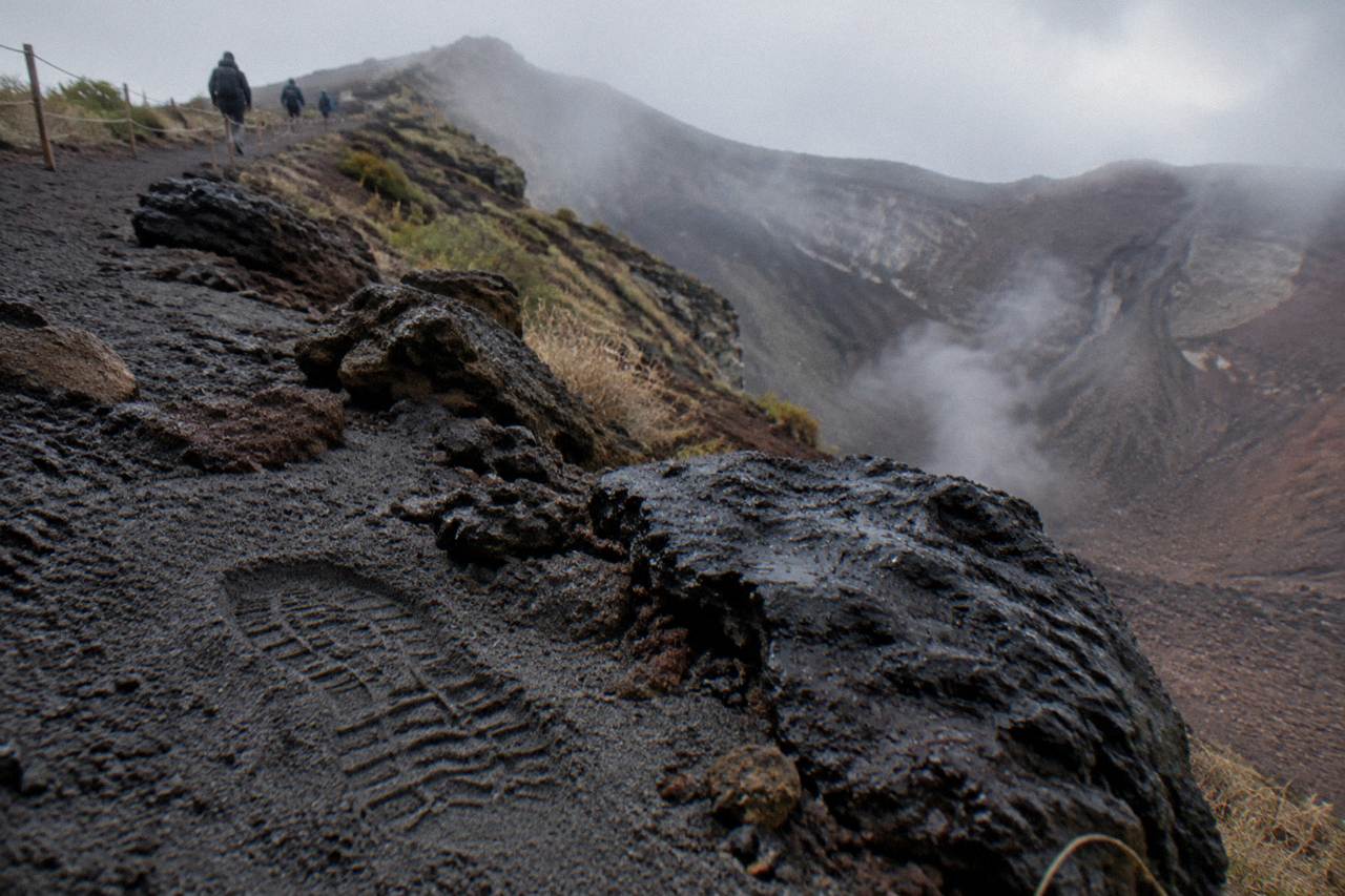 Dark volcanic rocks and ash along the crater rim path of Mount Vesuvius under a hazy sky
