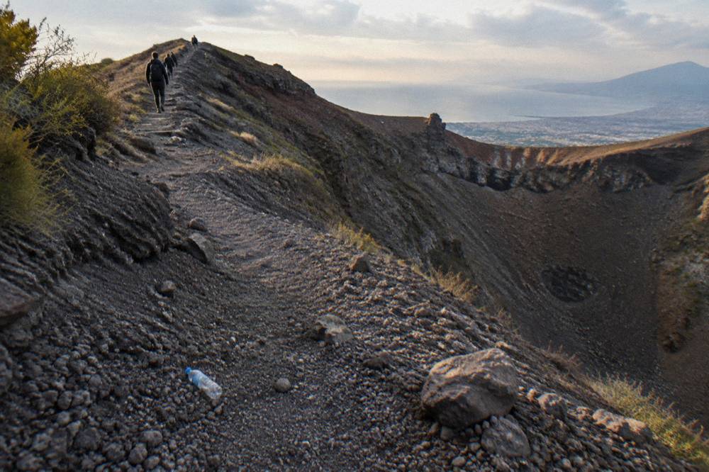 Winding footpath ascending loose volcanic slopes toward a wide crater rim under open sky