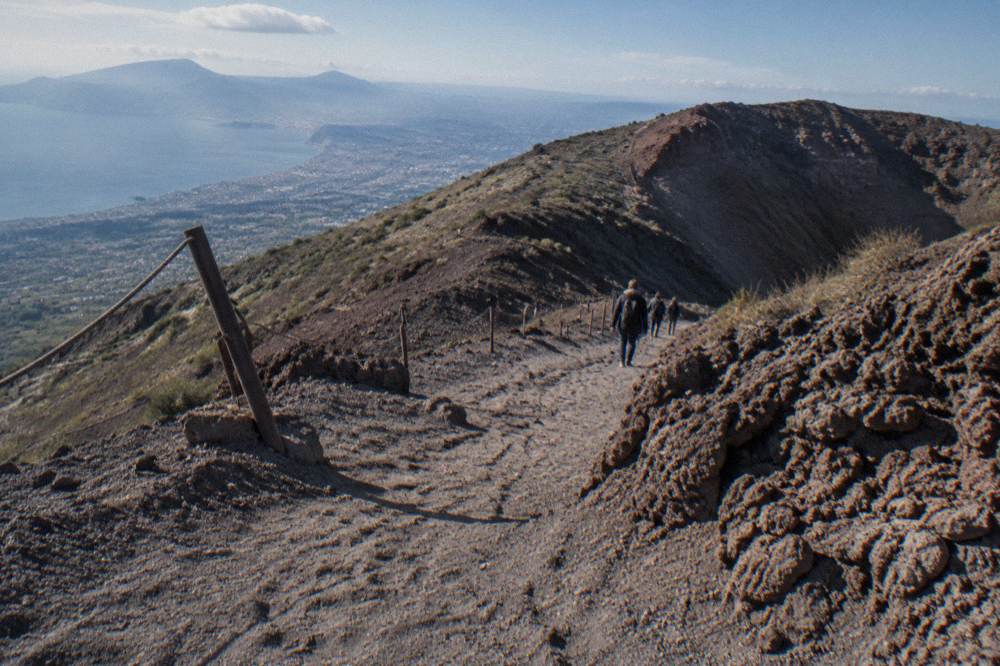 Sunlit ash path descending from the crater viewpoint with loose grey gravel