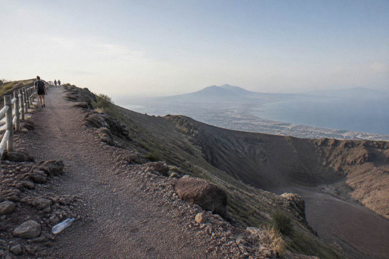 A dry volcanic crater rim path under a wide sky above the Bay of Naples