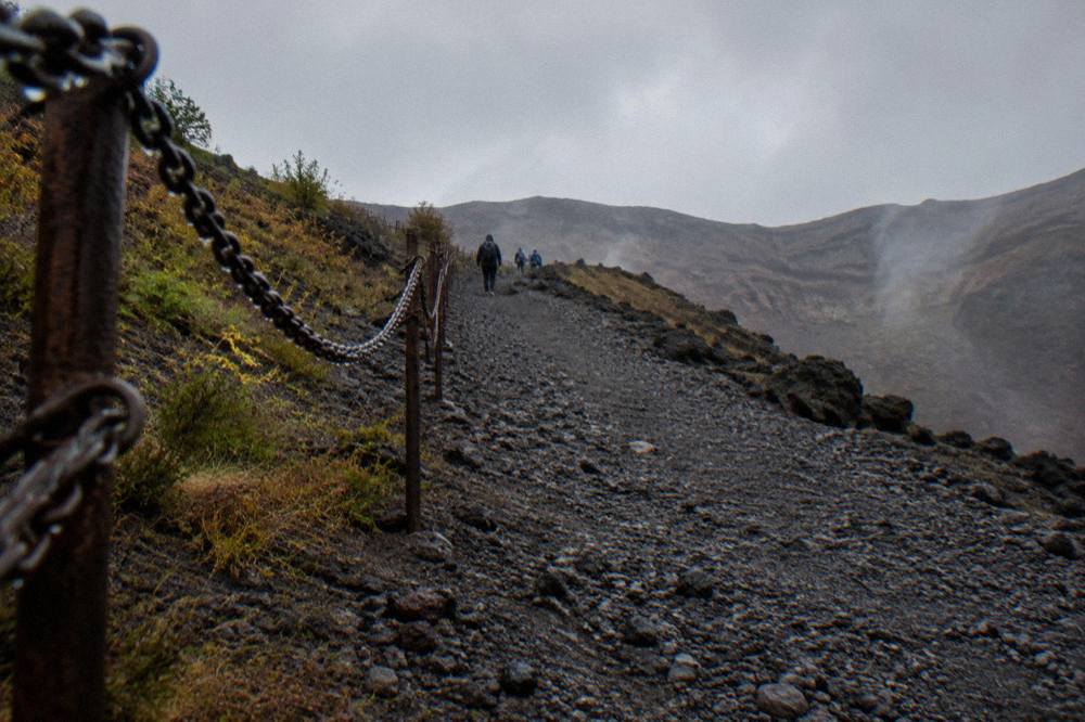 A view up the grey ash trail toward the Vesuvius crater rim with loose volcanic gravel on the path