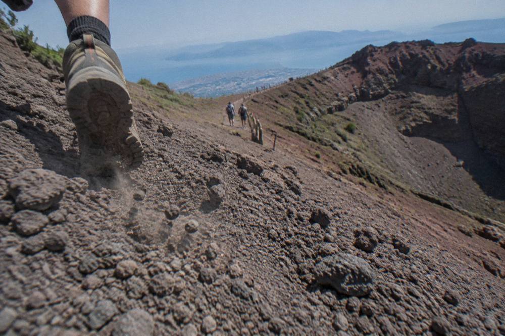Loose grey volcanic gravel path rising toward the crater rim with small stones rolling downhill