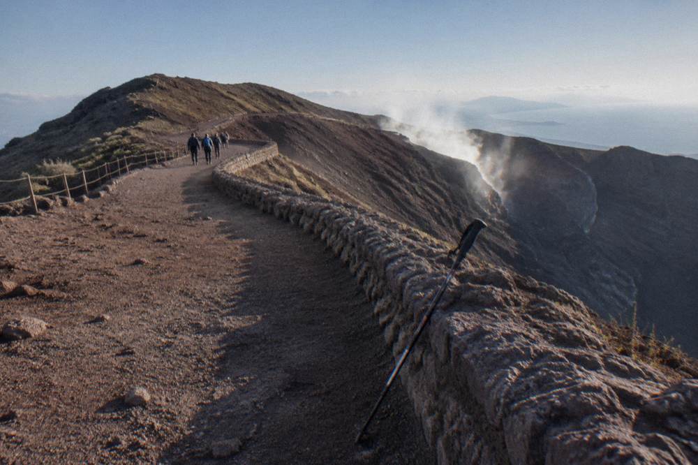 A wide volcanic ridge path curving toward the smoking crater edge under morning light