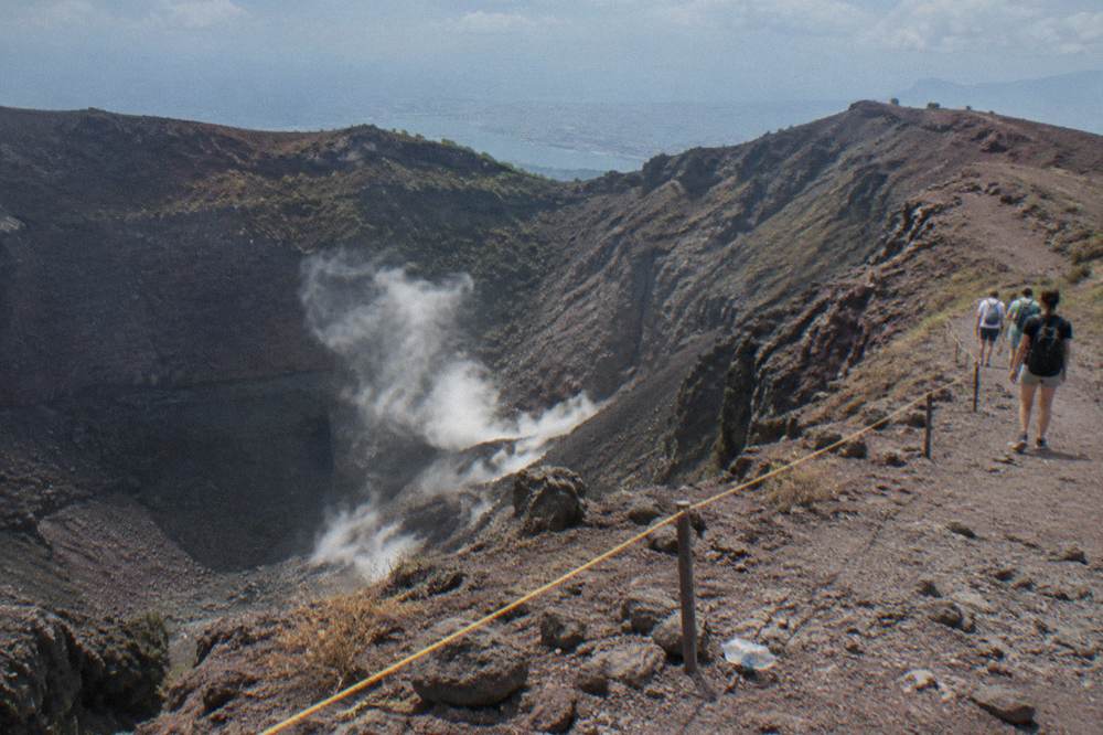 Visitors on the crater rim path of Vesuvius with steam rising from fumaroles inside the crater