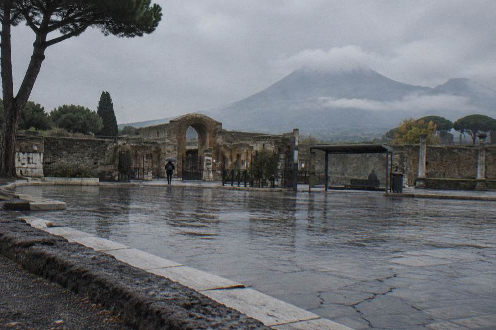 A stone-paved Roman street in Pompeii with worn cart ruts and Vesuvius on the horizon