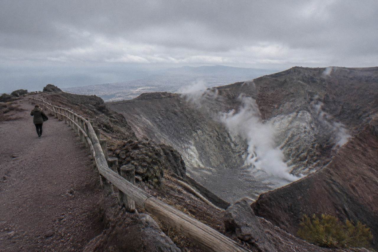 The crater of Mount Vesuvius under a grey sky with fumarole smoke on the inner walls