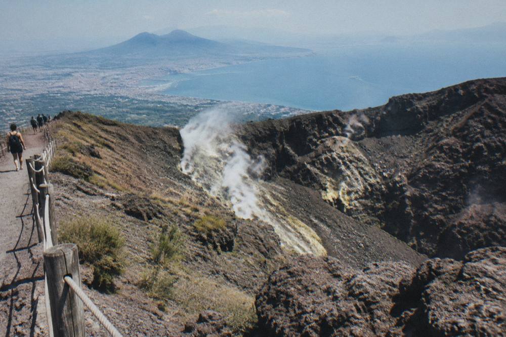 Vesuvius crater rim with steam rising from fumaroles and the Bay of Naples beyond