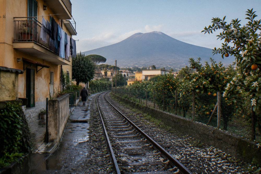 A single-track railway cutting through orange groves and towns on the slopes of Vesuvius
