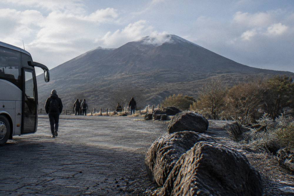 A regional bus parked at a mountain plaza with the volcanic cone rising behind it