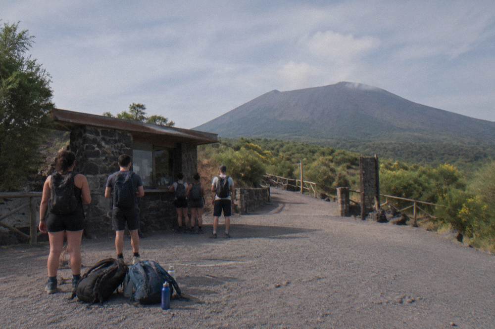The trailhead plaza on the volcano at morning with hikers gathering near a small ticket hut