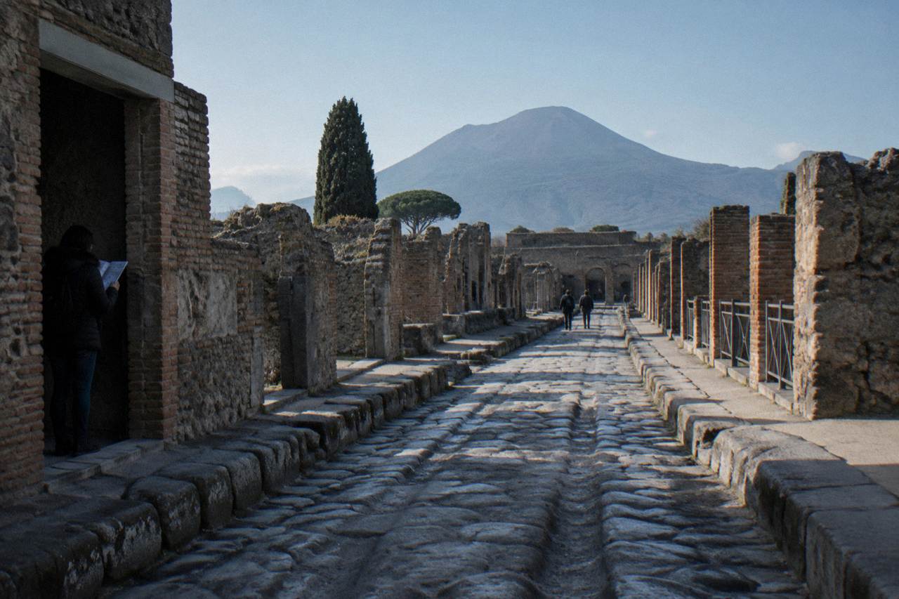 Ancient stone street in the Pompeii archaeological site with Mount Vesuvius rising in the background under a clear sky