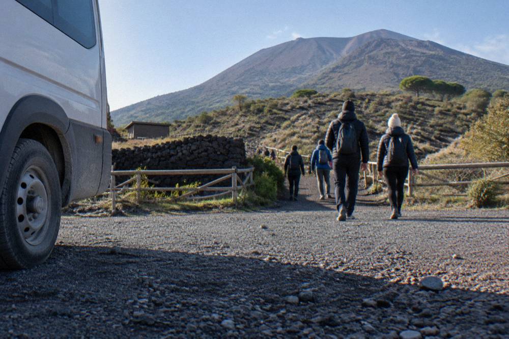 Hikers in jackets on the path toward the Vesuvius crater under a bright sky
