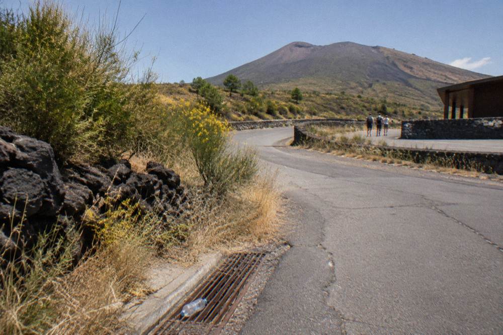 A winding asphalt road climbing through scrub and lava stone toward the upper slopes of the volcano