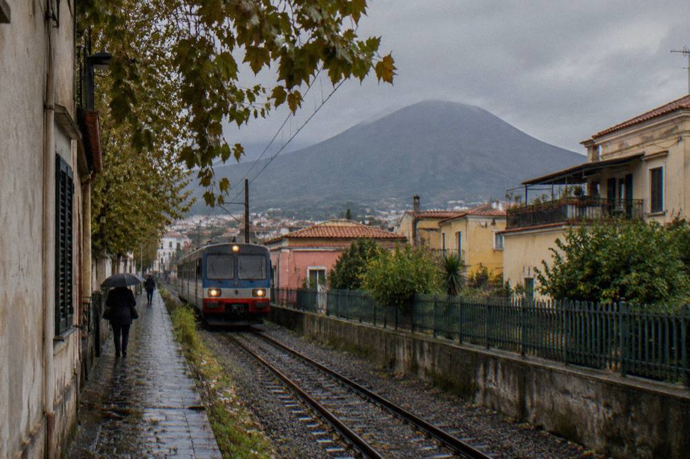 A single-track railway cutting through towns at the base of a volcanic mountain