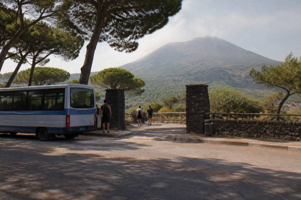 A small regional bus parked on a mountain road with volcanic slopes behind it