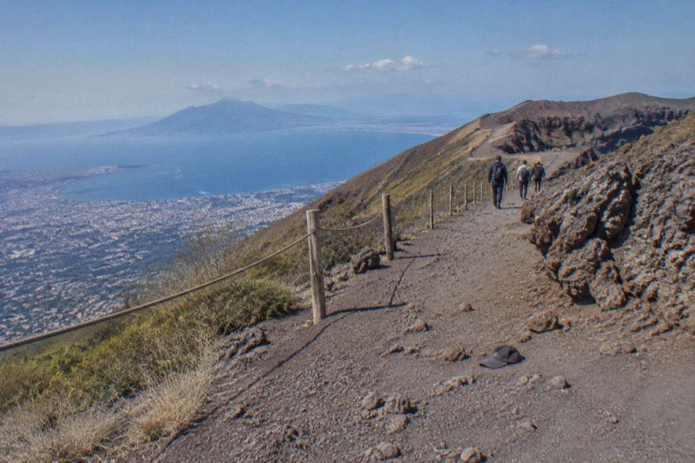 Hikers walking along the crater rim path on Mount Vesuvius with the Bay of Naples in the distance