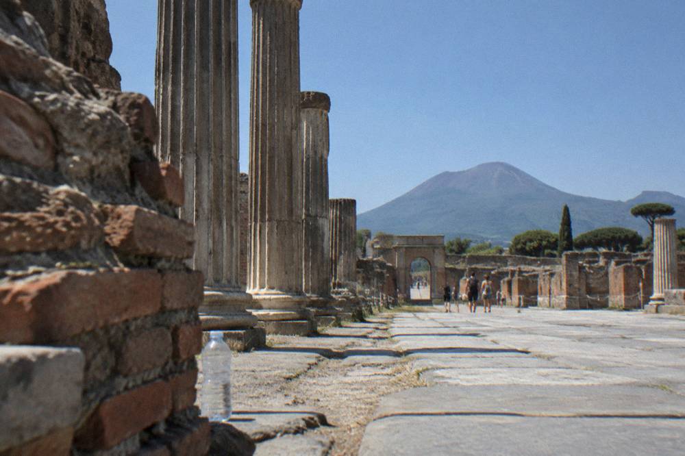 Columns of the Pompeii forum standing against a bright sky with ancient wall fragments in the foreground