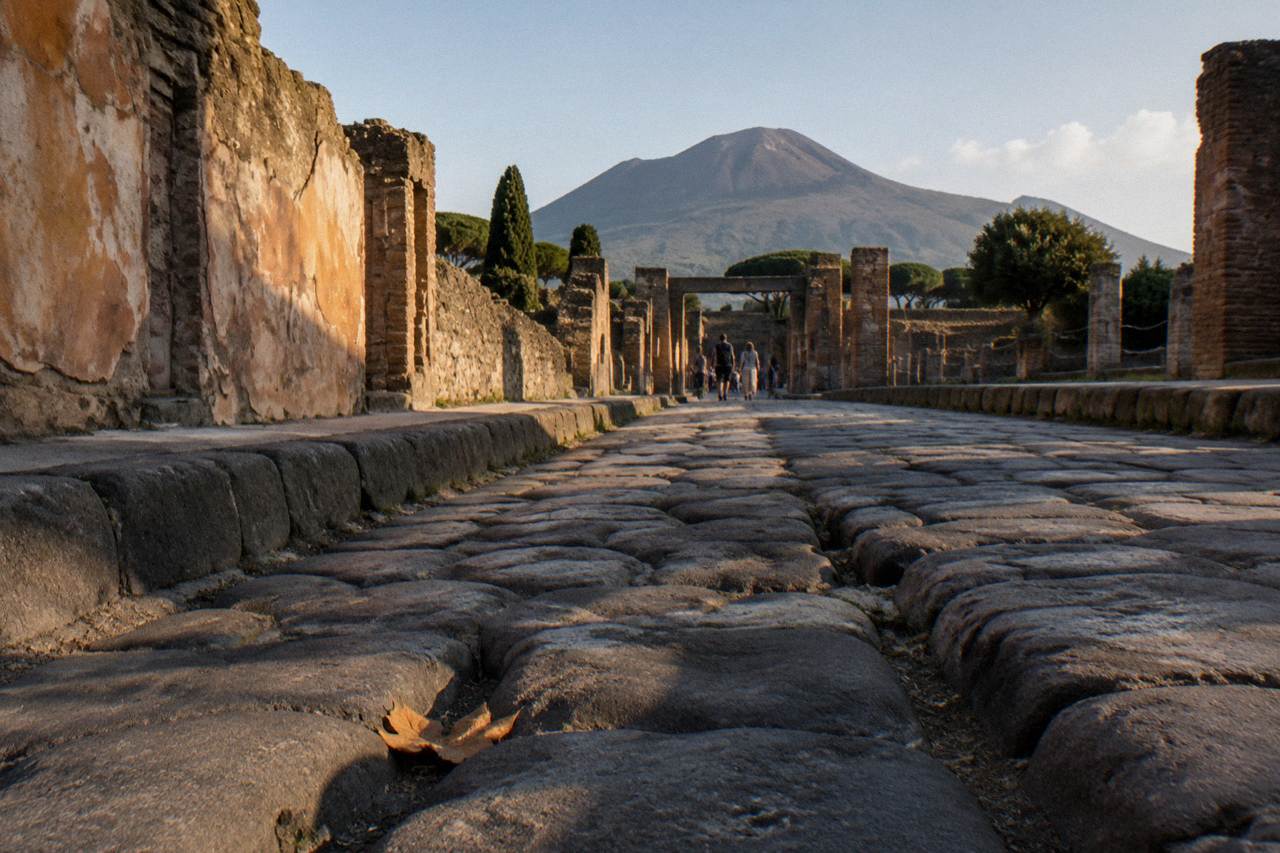 Stone-paved Roman street in Pompeii with worn cart ruts and crumbling plastered walls under a clear sky