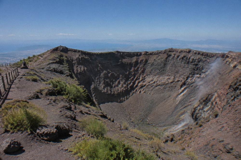 The wide crater of Mount Vesuvius under a clear sky with a walking path along the rim