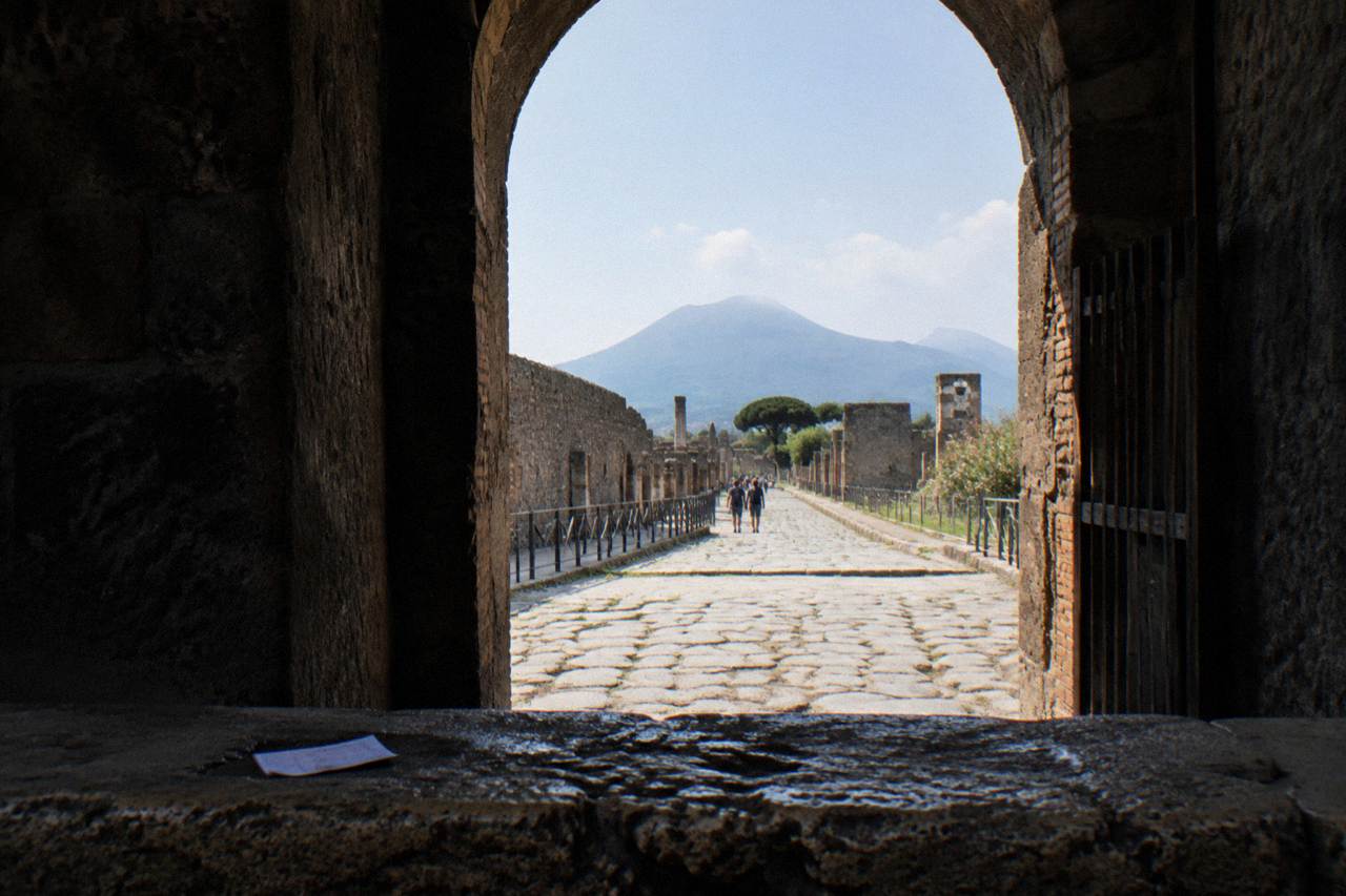The stone columns of the Pompeii forum under a clear morning sky with Vesuvius rising in the background