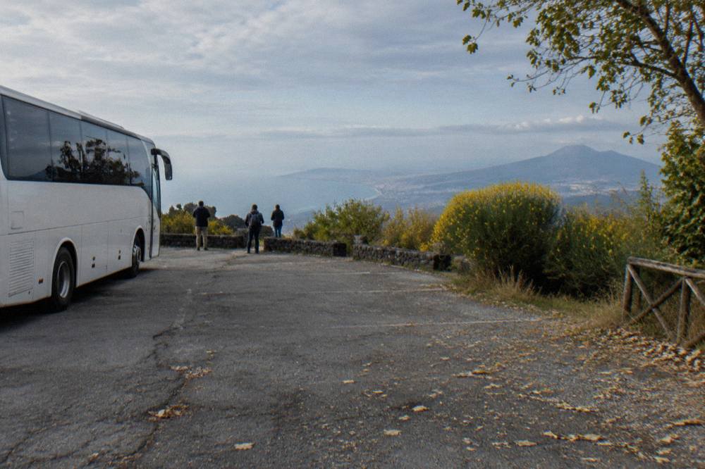 Tour bus parked on the Vesuvius park road with the crater ridge and bay of Naples in the distance