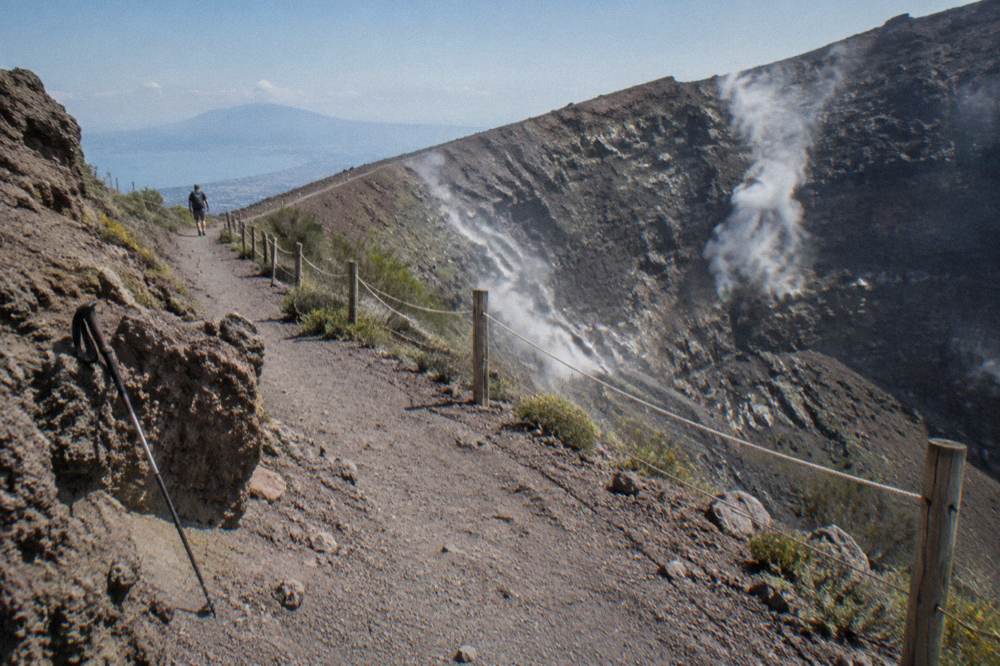 Vesuvius crater rim path with steam rising from fumaroles on the dark inner walls
