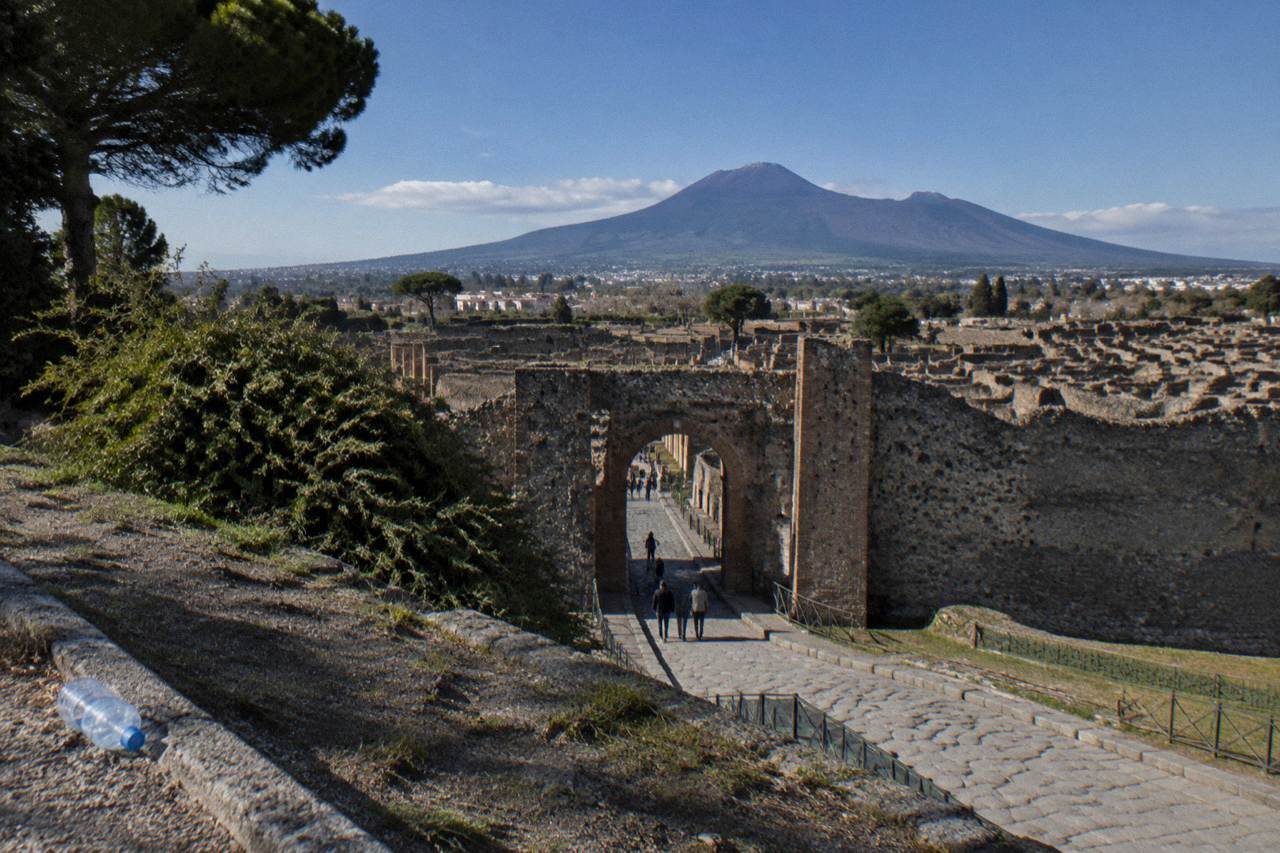 Stone street in ancient Pompeii with Mount Vesuvius rising behind under a blue sky