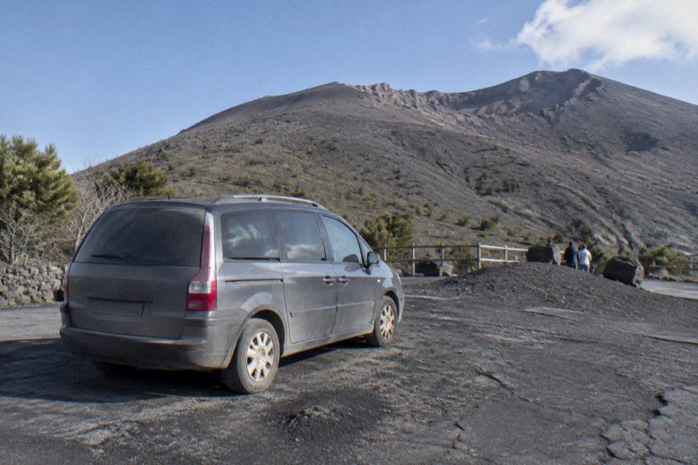 A minivan parked at the Vesuvius trailhead with the volcano slope behind it