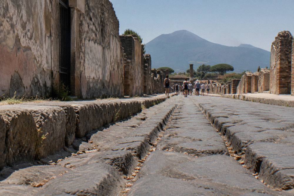 The stone-paved main street of Pompeii with worn wheel ruts and ruined walls on both sides
