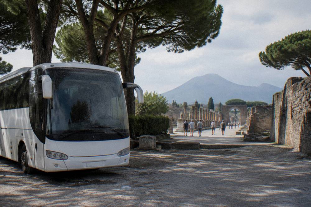 A tour coach parked on a tree-lined road beside the ancient walls of Pompeii