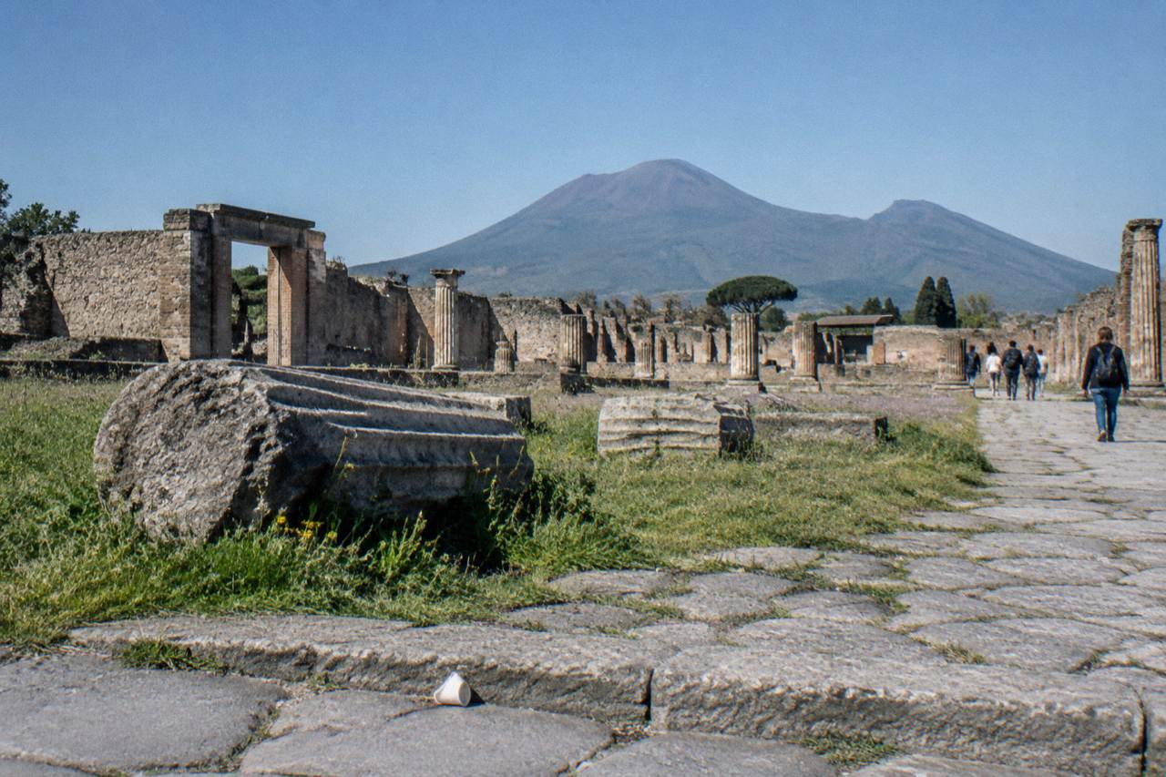 Stone columns of the Pompeii forum with Mount Vesuvius rising in the background under a clear sky