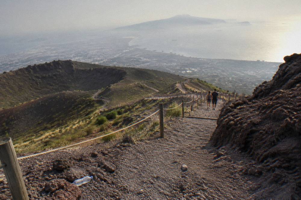 The wide gravel crater path winding uphill with the Bay of Naples hazed in the distance