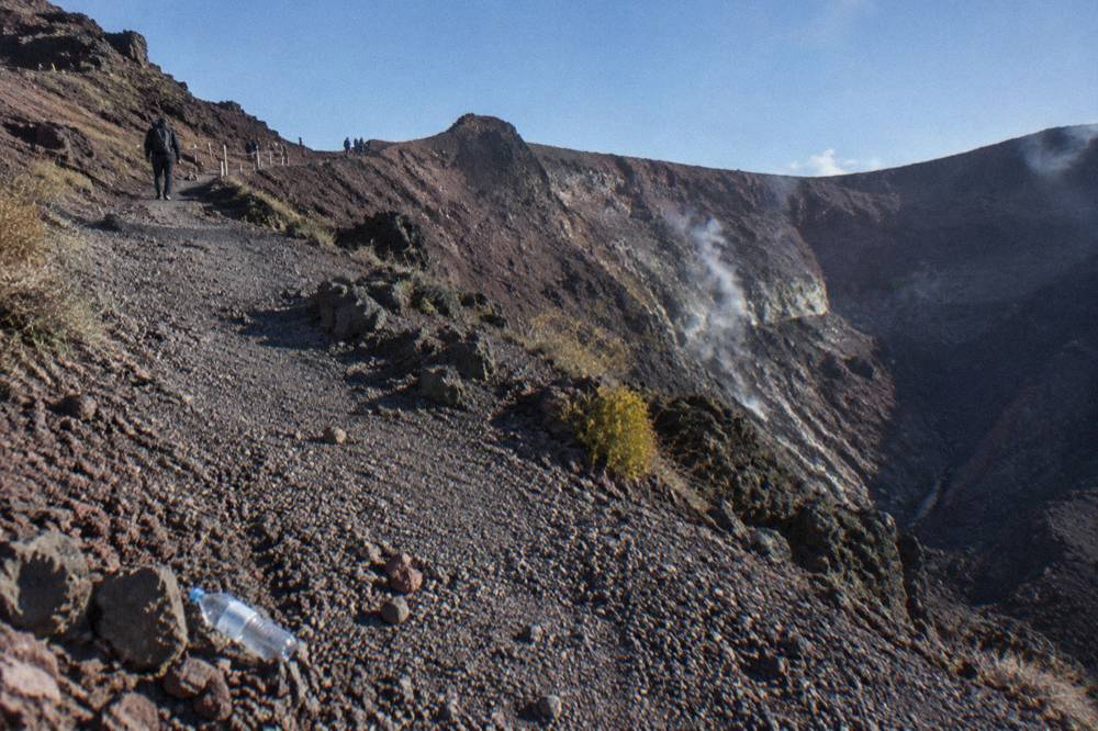 The gravel crater path of Mount Vesuvius climbing toward the rim with steam vents on the inner walls