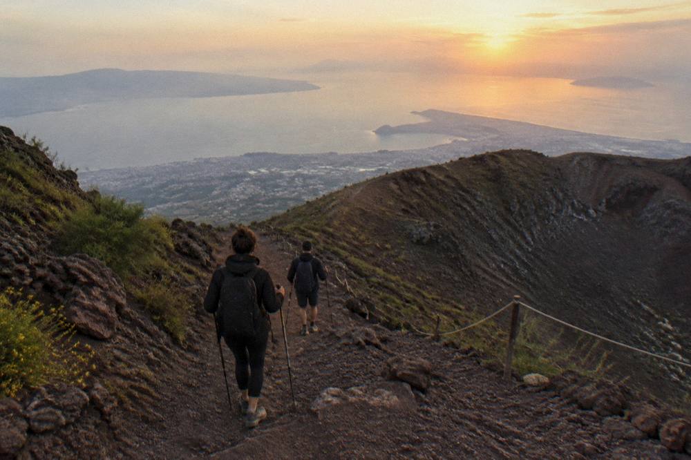 Hikers descending the Vesuvius crater path with the Bay of Naples and Sorrento peninsula in the distance