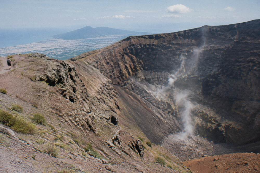 Wide crater of Vesuvius with steam rising from the inner walls under a blue sky