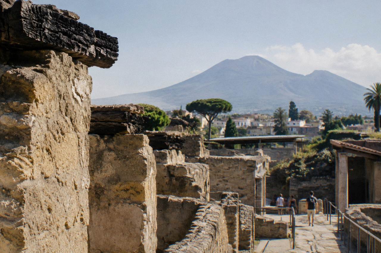 Stone ruins of ancient Herculaneum under a clear sky with Mount Vesuvius rising in the background