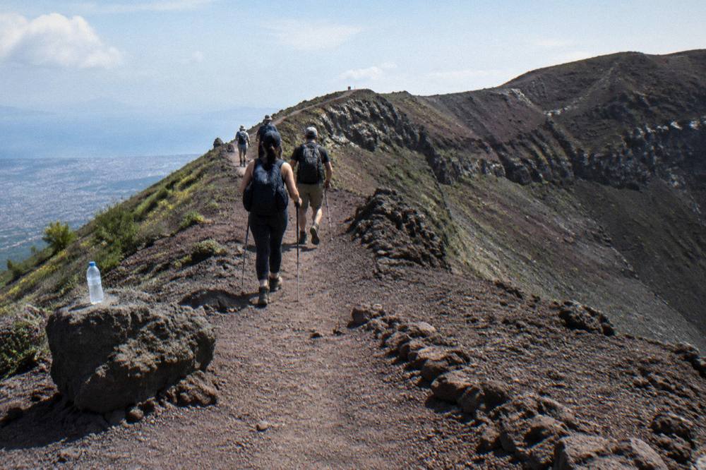 Hikers in sturdy shoes walking the dusty crater path toward the Vesuvius rim
