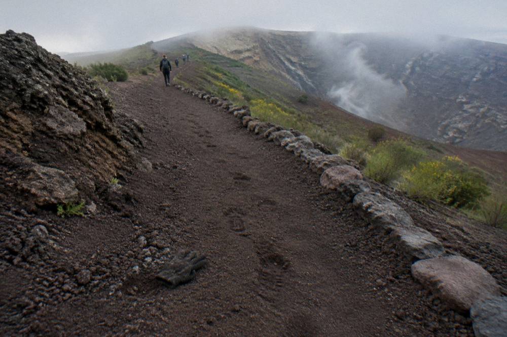 A stone trail winding up through dark volcanic ash toward a wide crater rim under an open sky