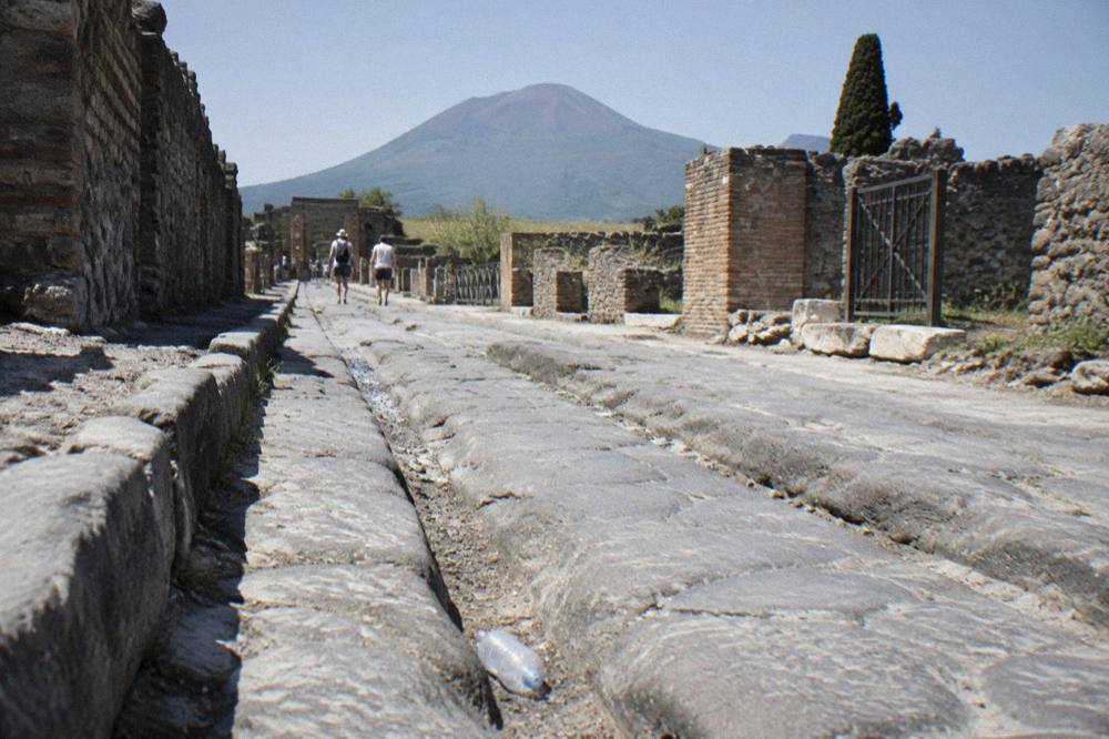 Ancient stone street with worn cart ruts between ruined walls under bright midday sun