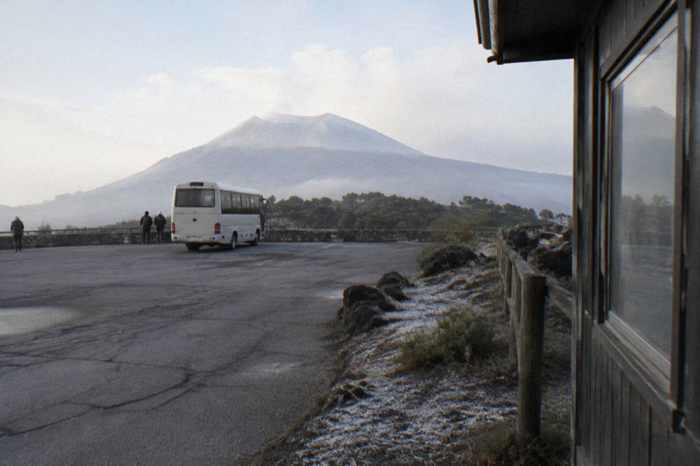 A small coach parked at a viewpoint car park above the tree line on Vesuvius